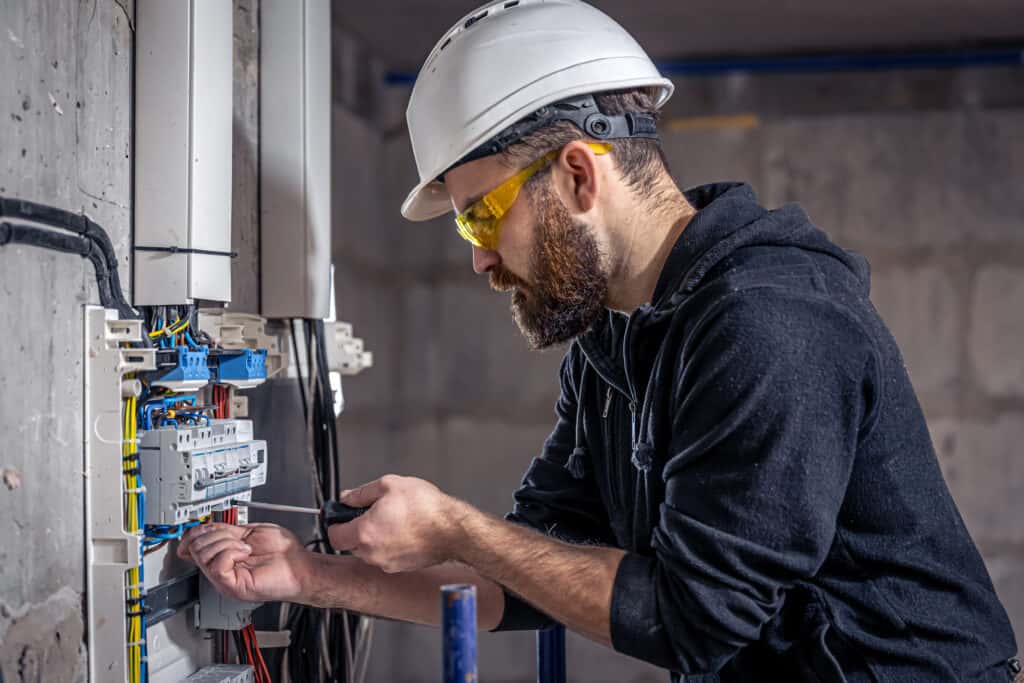 Un electricista masculino trabaja en un cuadro de distribución con un cable de conexión eléctrica